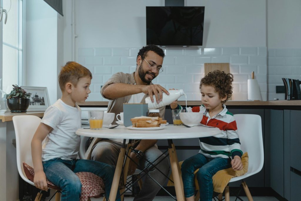 Der Vater schenkt seinen Söhnen beim Frühstück zu Hause Milch ein und fördert so den Zusammenhalt der Familie.
