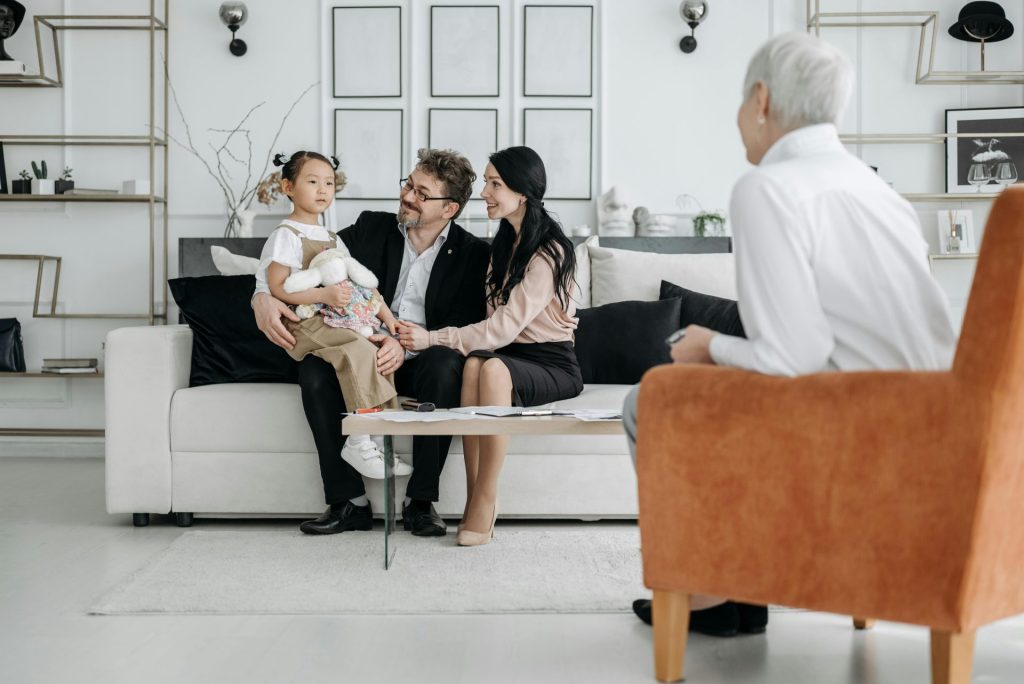 Eine Familie trifft sich in einem gemütlichen Wohnzimmer mit einer Sozialarbeiterin, um Einzelheiten der Adoption zu besprechen.