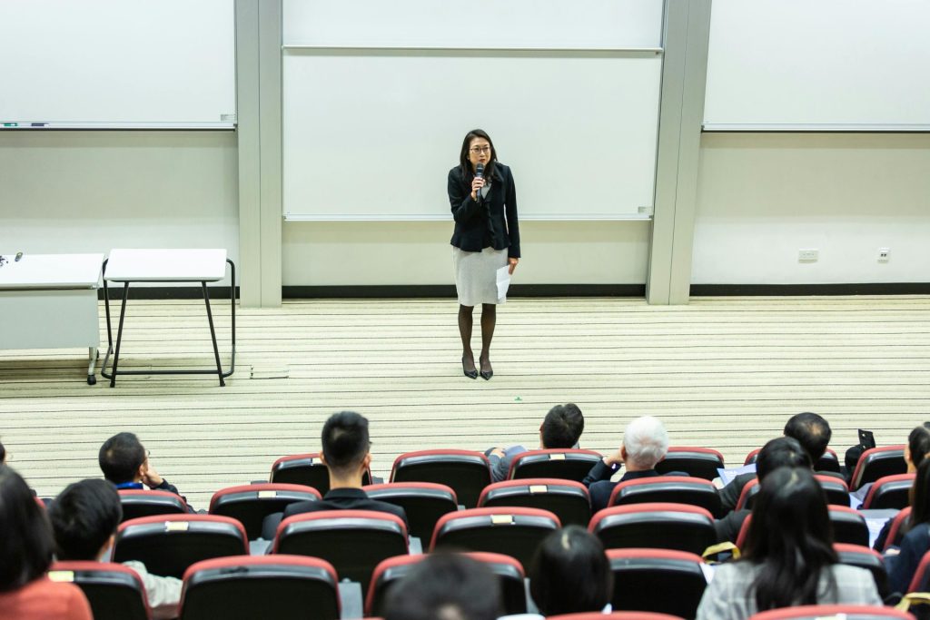 Eine Rednerin hält einen Vortrag vor Publikum in einem modernen Auditorium.