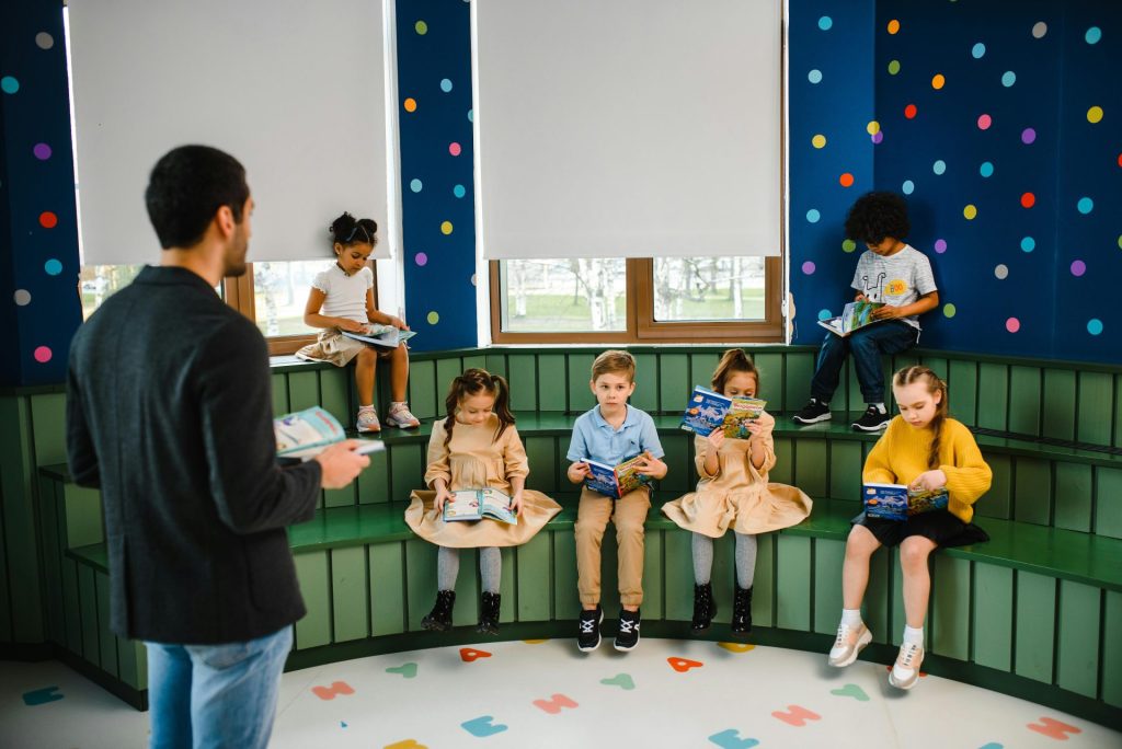 Eine Vorschullehrerin leitet die Vorlesestunde mit Kindern in einem farbenfrohen Klassenzimmer.
